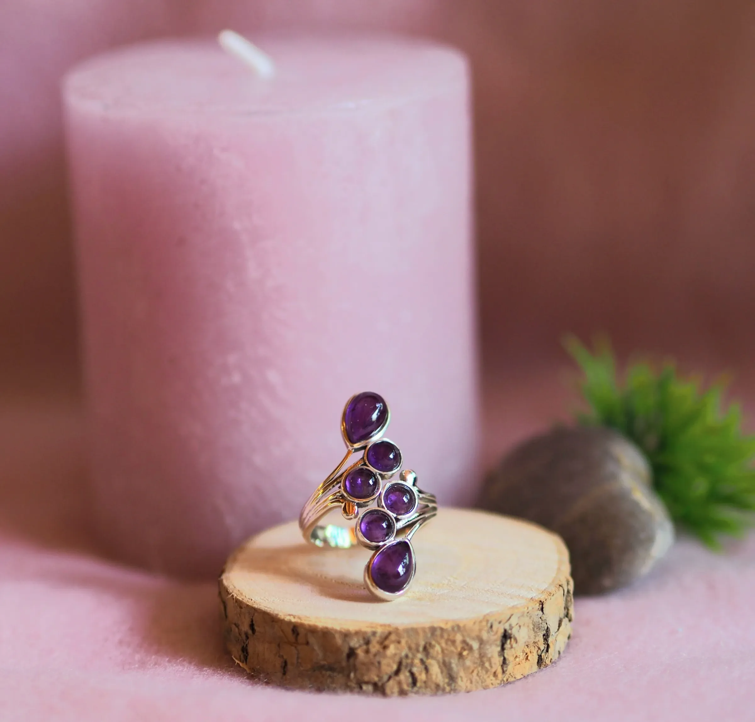 Bague en argent ornée de six cabochons d’améthyste violette alignés en courbe, posée sur une rondelle de bois devant une bougie rose