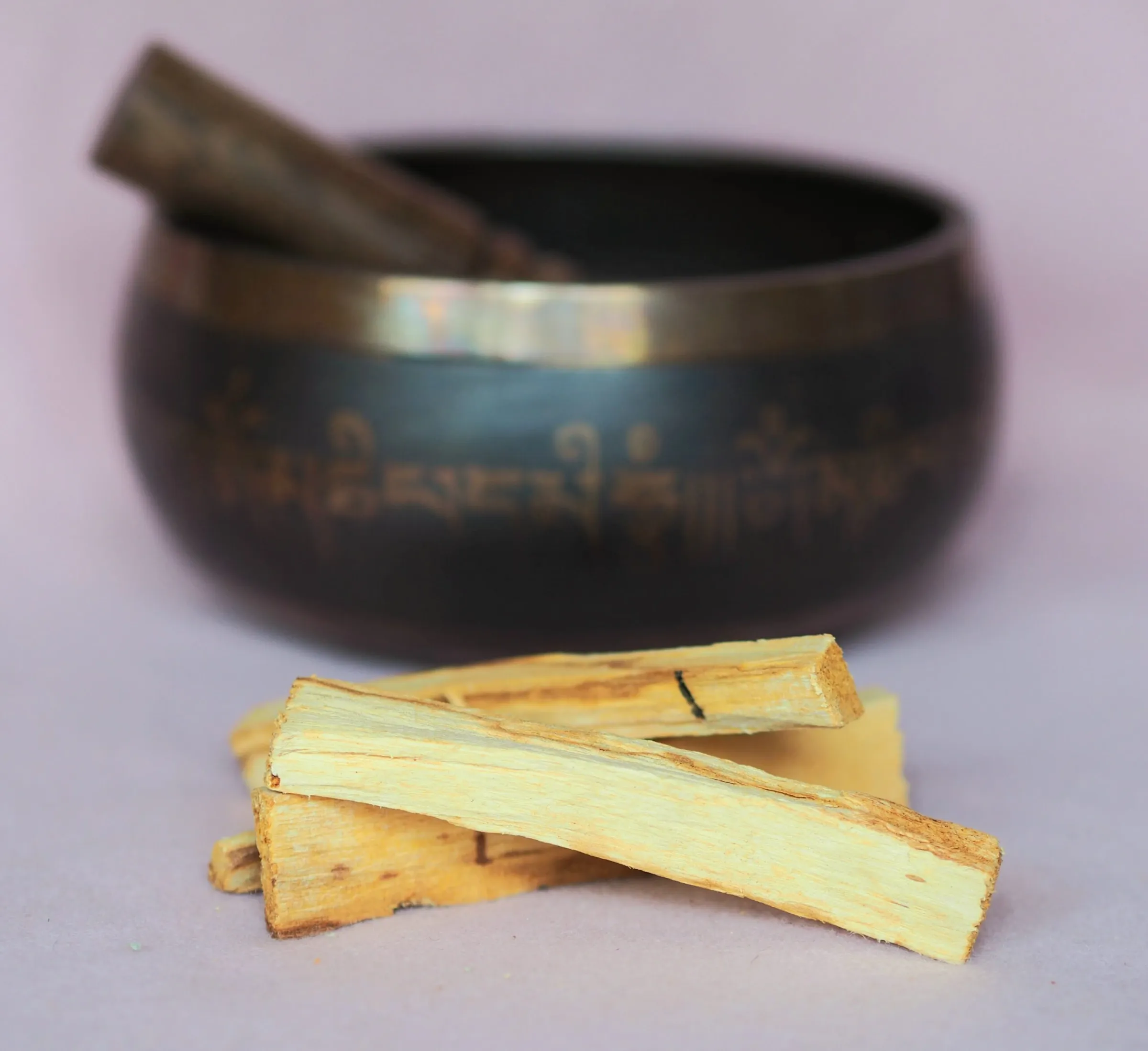 Bâtons de palo santo au bois clair, posés en tas devant un bol chantant