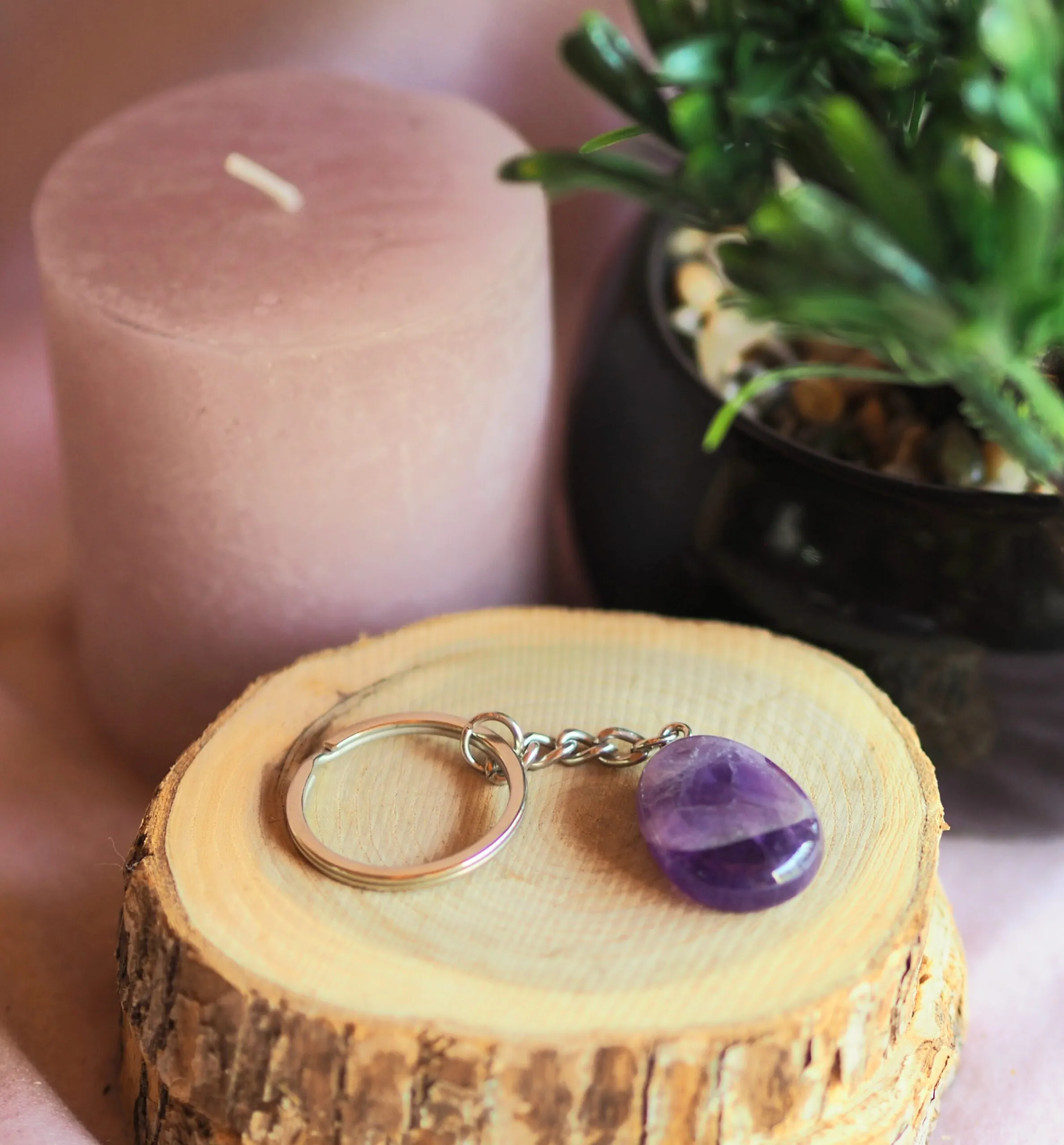 Porte-clés en améthyste violette, pierre plate sur une chaînette et un anneau argentés, posé sur une rondelle de bois près d’une bougie