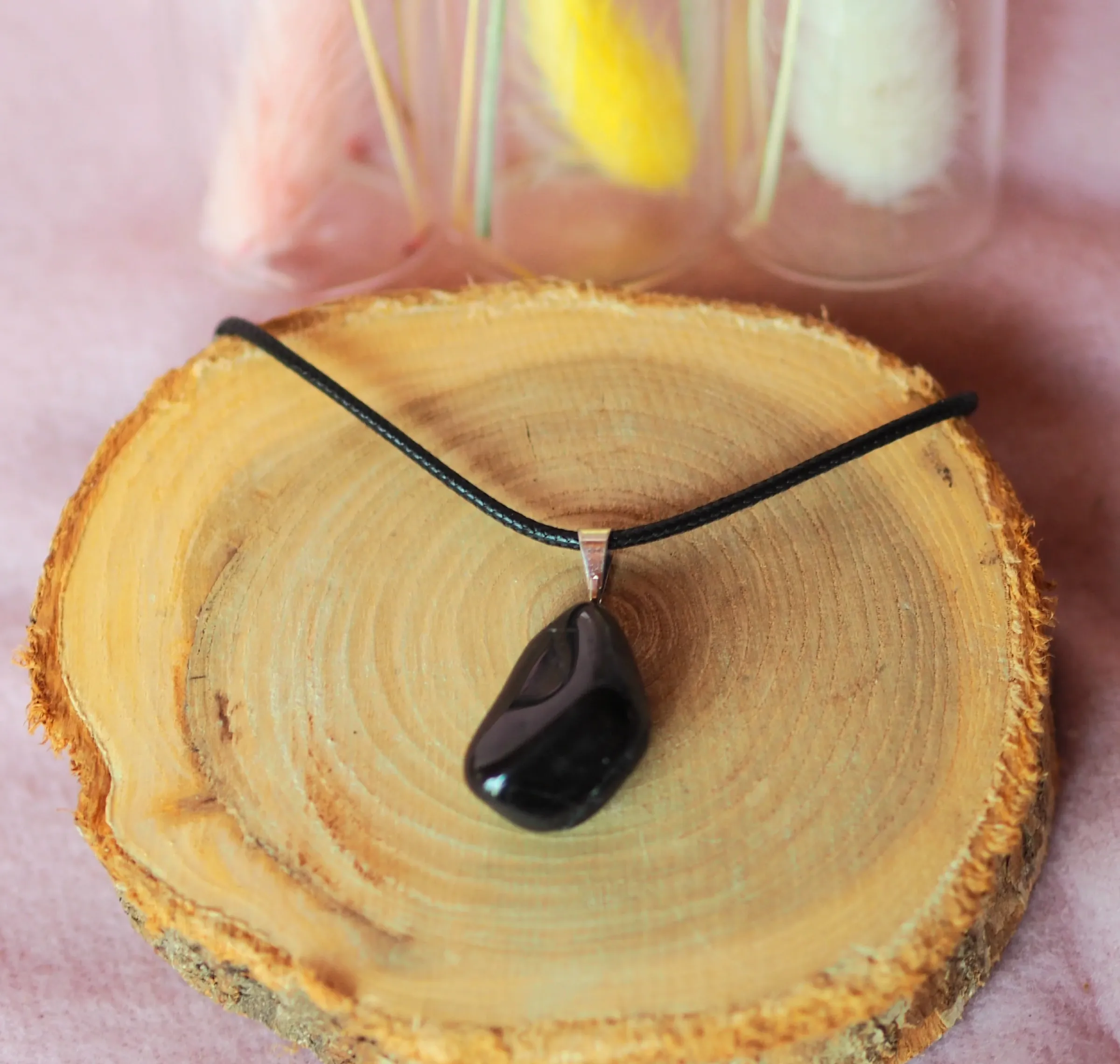 Pendentif en tourmaline noire polie, avec une bélière argentée sur un cordon de cuir noir, posé sur une rondelle de bois