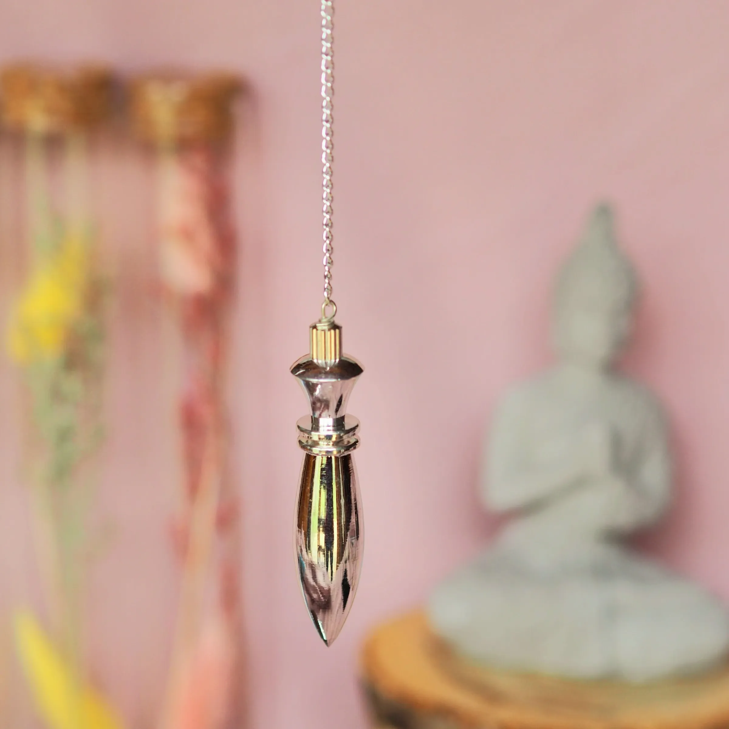 Pendule argenté de style égyptien, tête ouvragée et corps fuselé terminé en pointe, suspendu à une chaînette