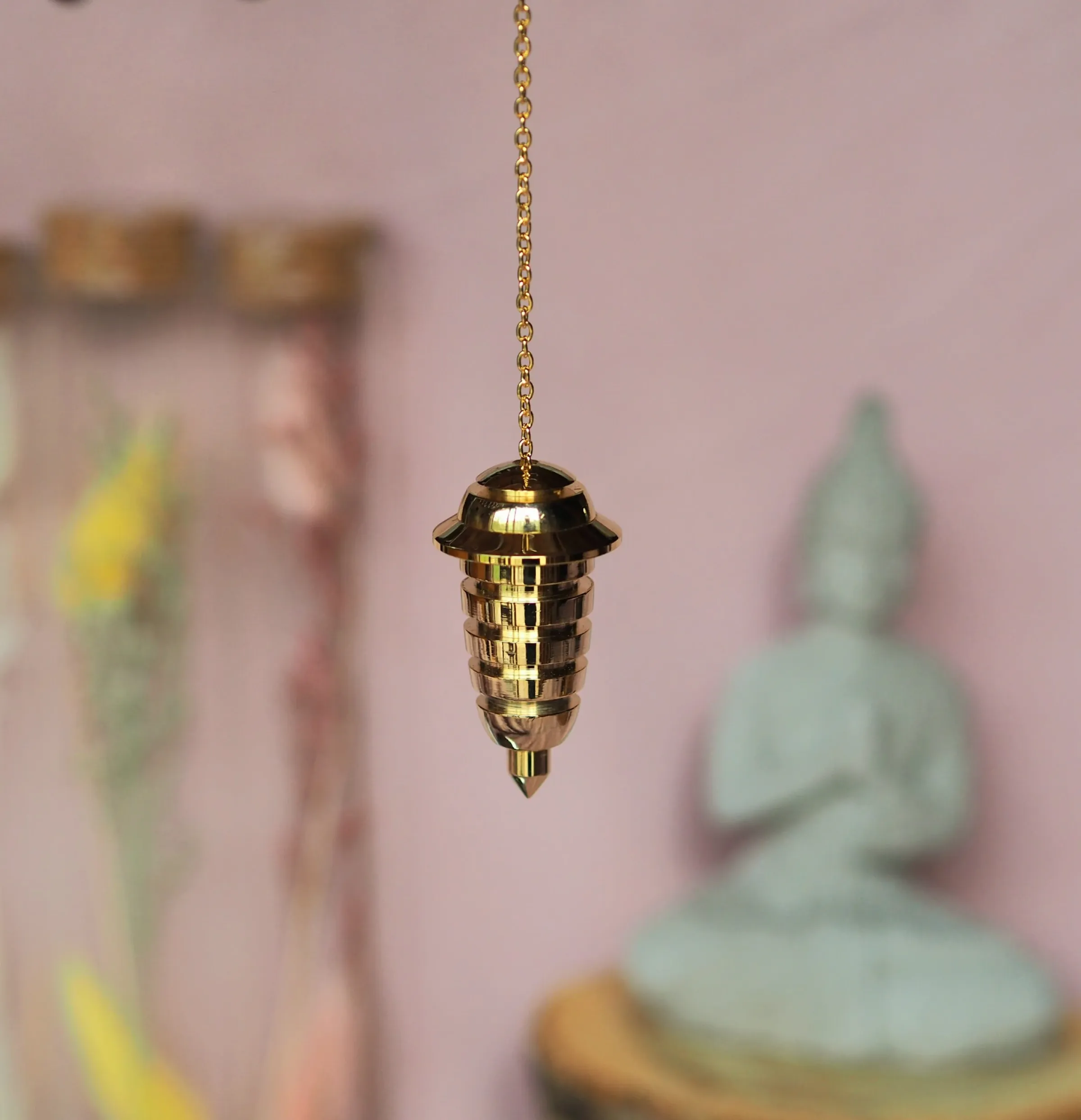Pendule doré en forme de pagode, chapeau évasé et corps strié d’anneaux, suspendu à une chaînette dorée