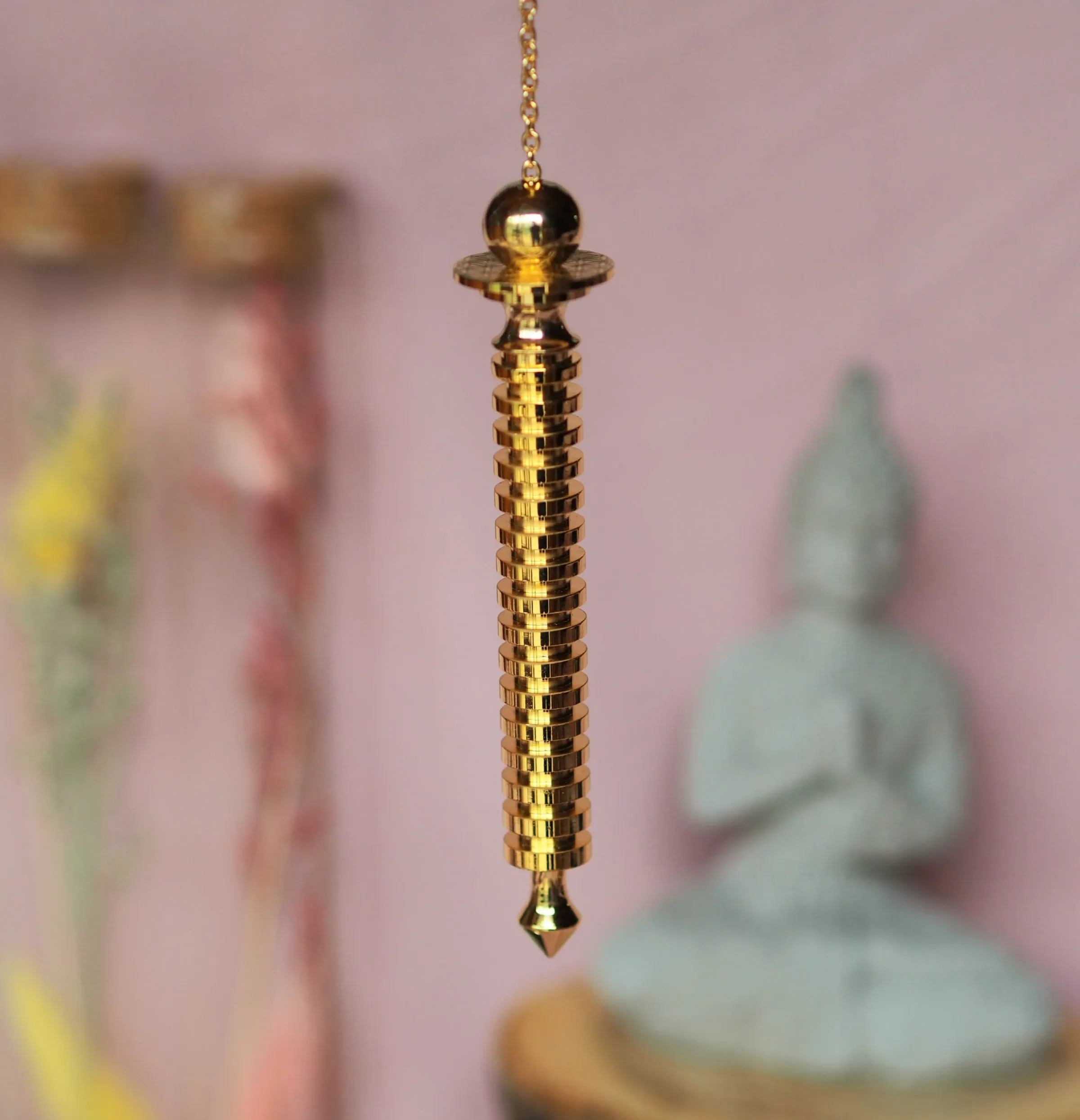 Pendule doré en forme de longue colonne cannelée, terminé par une pointe et suspendu à une chaînette dorée