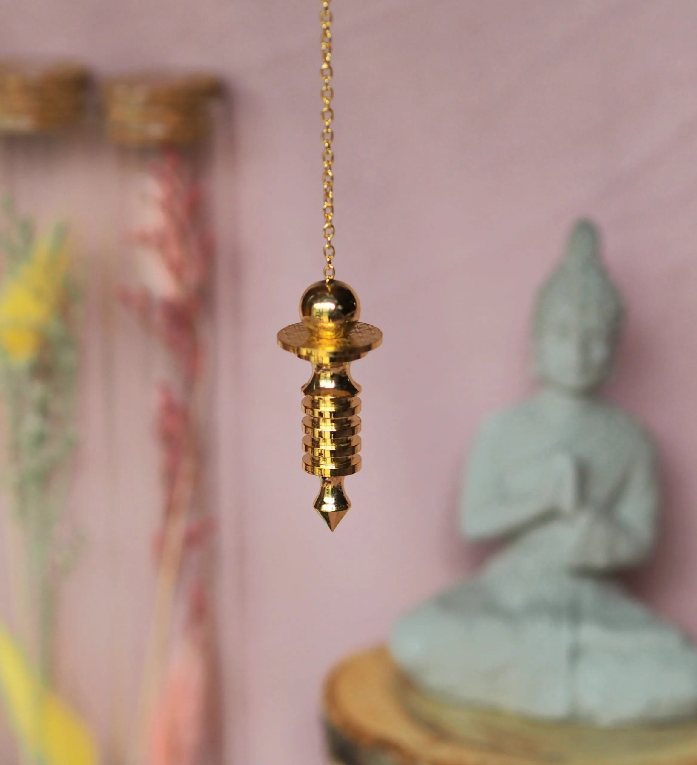 Pendule doré avec une sphère, un disque et des anneaux superposés terminés par une pointe, suspendu à une chaînette dorée