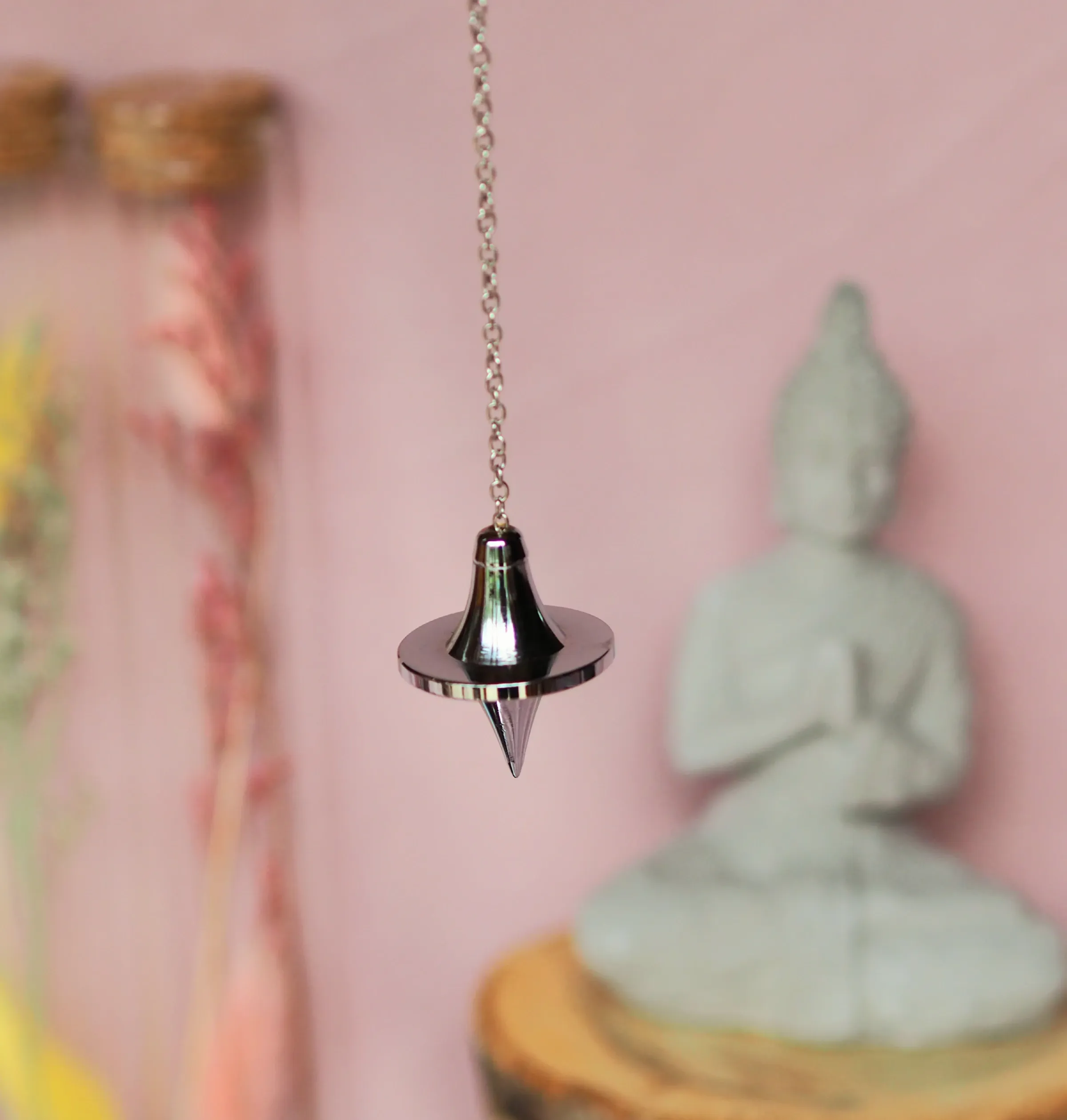 Pendule chromé à large disque, entre une tête en cloche et une pointe conique, suspendu à une chaînette