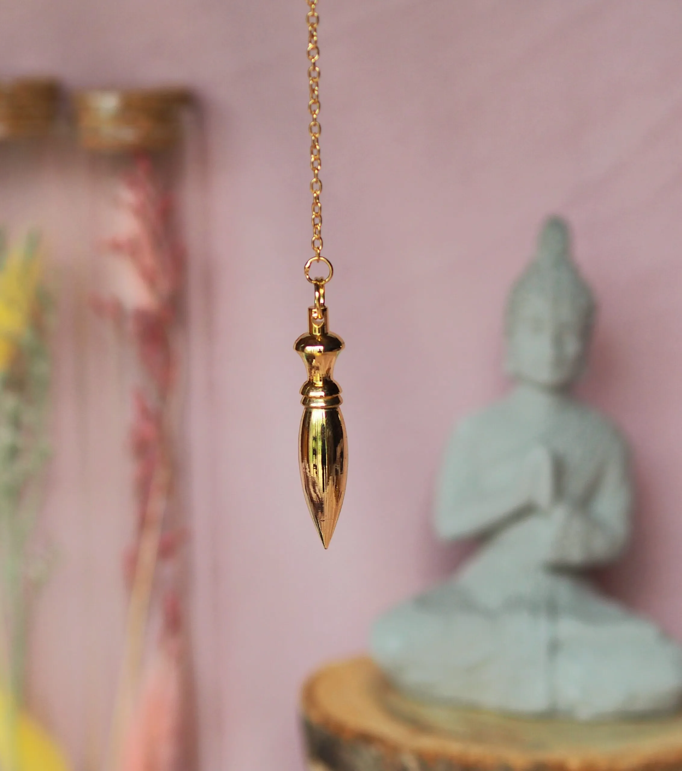 Pendule doré allongé, à la tête ouvragée et au corps lisse effilé en pointe, suspendu à une chaînette dorée