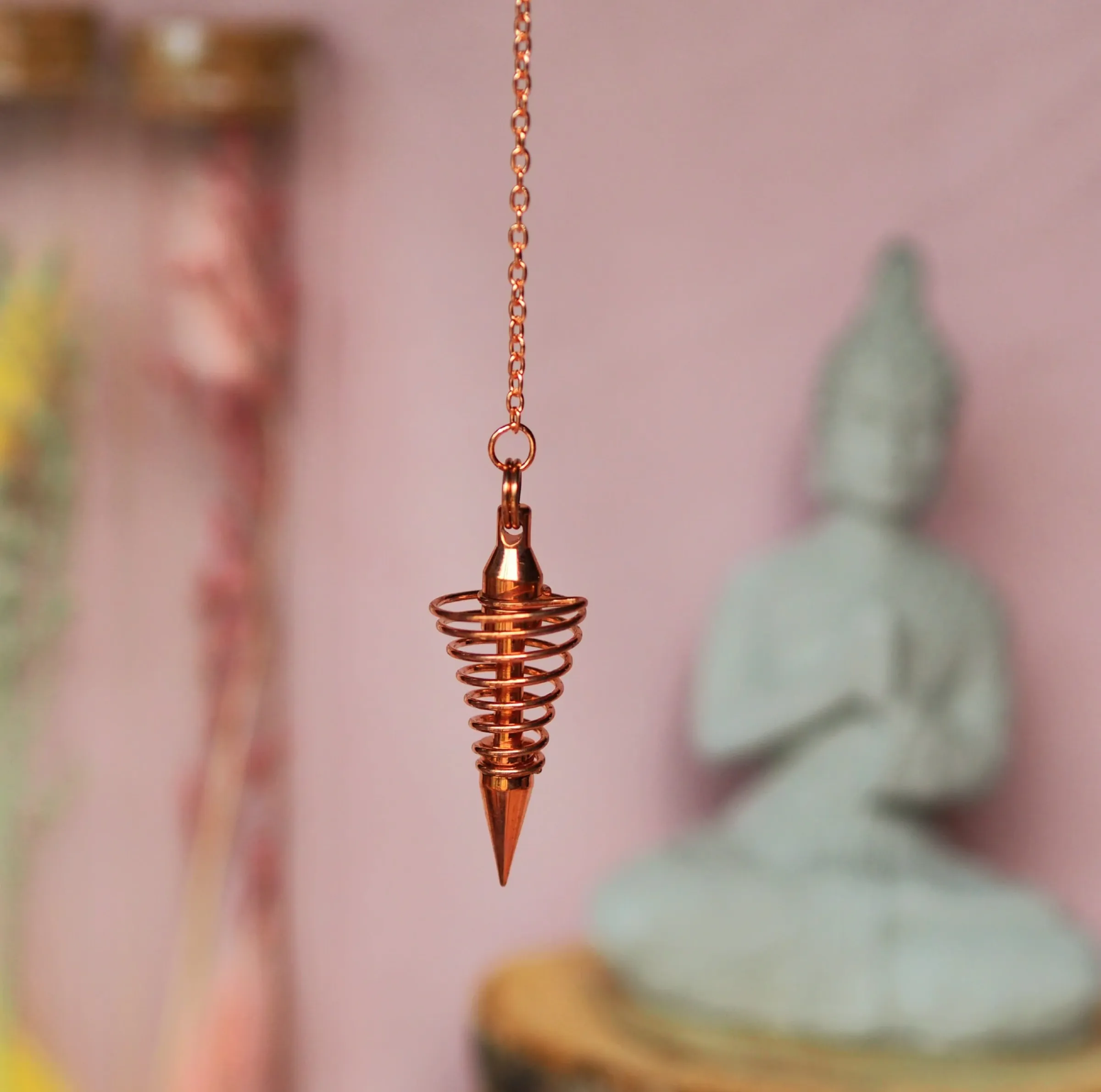 Pendule en spirale aux reflets cuivrés qui se resserre vers une pointe, suspendu à une chaînette cuivrée
